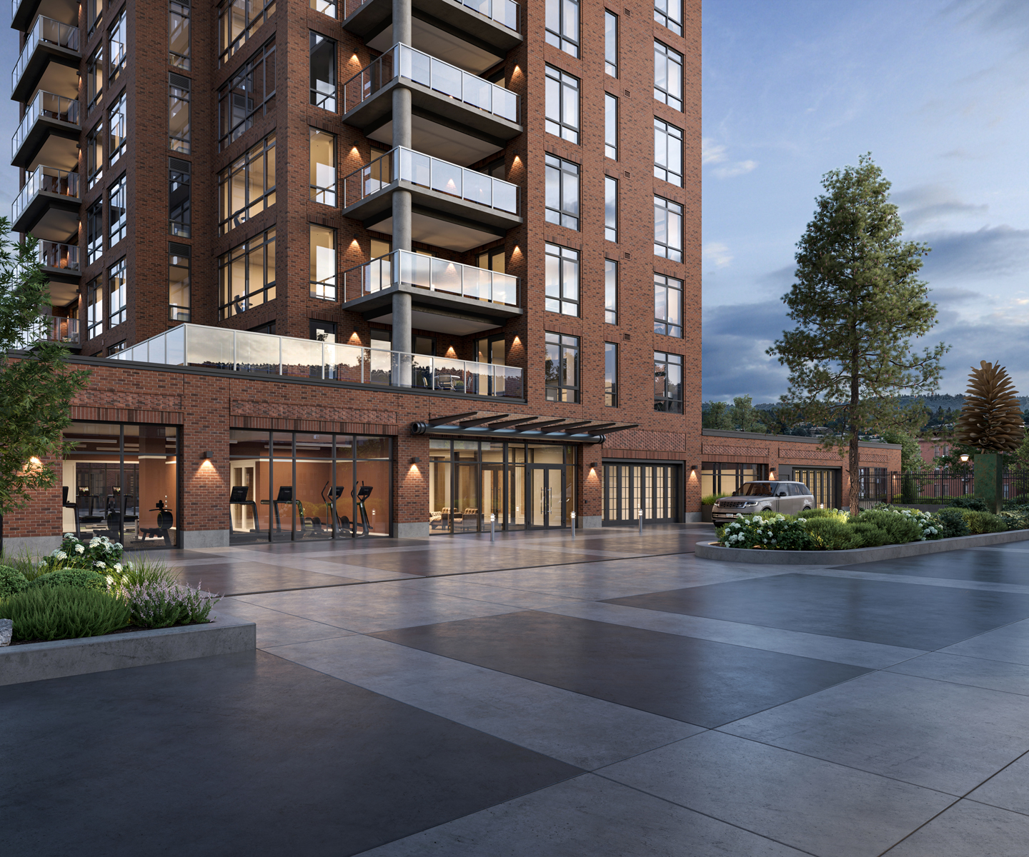Exterior view of Spokane Falls Tower at dusk, showing the main entrance, fitness center, landscaped plaza, secure parking access, and modern brick architecture with glass balconies.