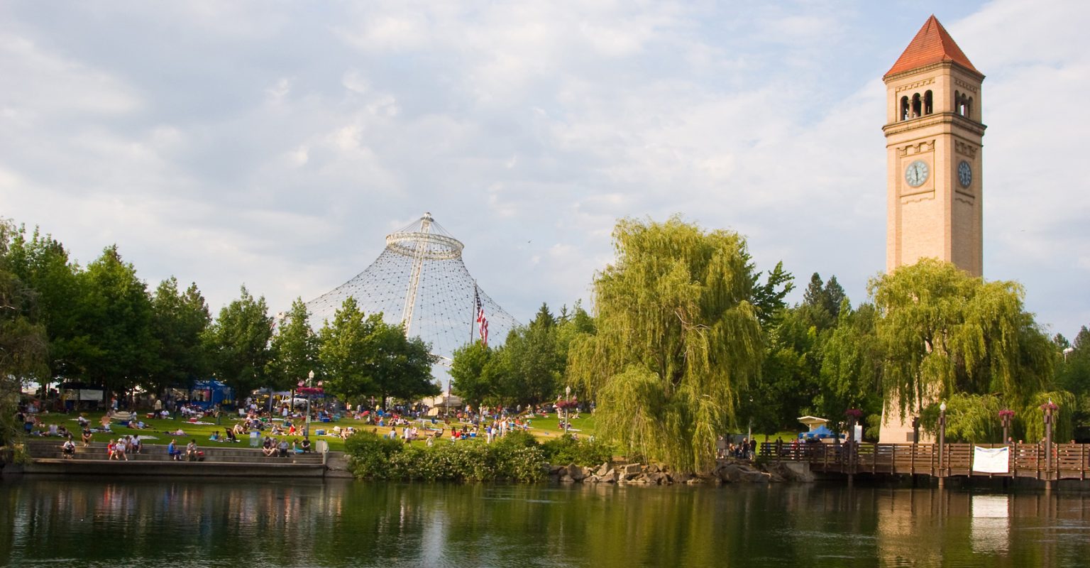 Riverfront Park in downtown Spokane, featuring the Clock Tower, Pavilion structure, trees, and the Spokane River along the park’s edge.